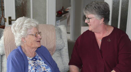 Two ladies wearing glasses sitting side-by-side and chatting