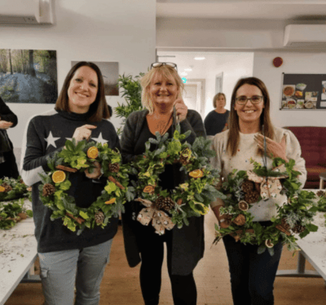 Three participants holding their completed Christmas wreaths