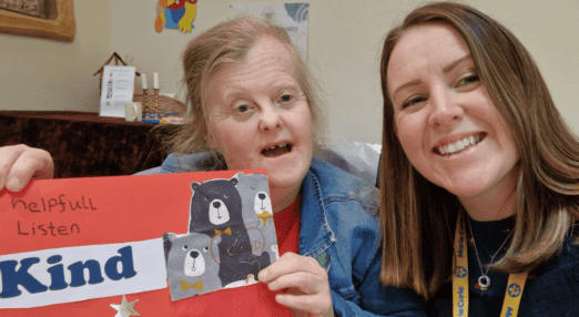 Two people smiling with person on the left holding a poster that says Kind