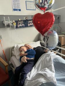 man lying in IPU with balloons and son