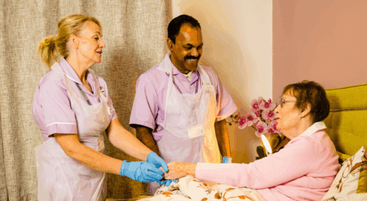 two healthcare assistants helping a patient smiling
