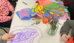 a group of people sitting at a table covered in art supplies