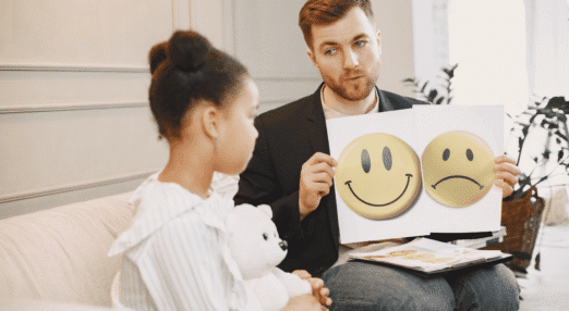 Copilot said: Volunteer supporting a child using emotion cards to talk about feelings during a one-to-one session.