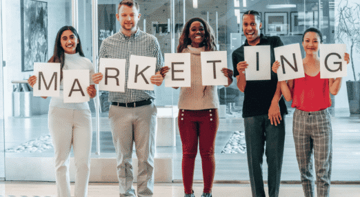 Group holding letters spelling “MARKETING” in an office setting.